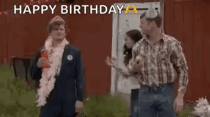 A Group Of People Are Standing In Front Of A Red Barn And One Of Them Is Wearing A Party Hat . GIF