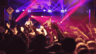 A Group Of People Are Standing In Front Of A Stage That Has The Word Tropicals On It GIF