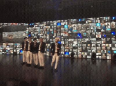 A Group Of People Are Standing In Front Of A Wall Of Pictures GIF