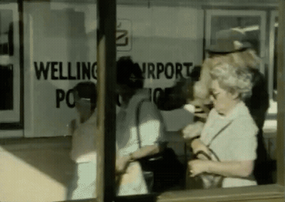 A Group Of People Are Standing In Front Of A Welling Airport Sign GIF