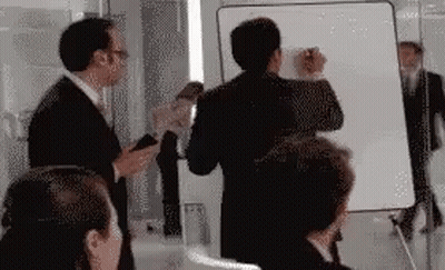 A Group Of People Are Standing In Front Of A White Board . GIF