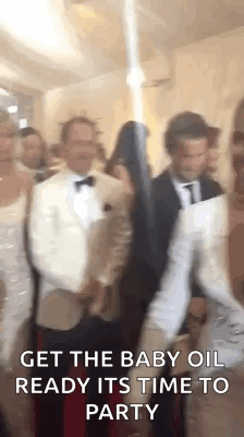 A Group Of People Are Standing Next To Each Other In A Room And One Of Them Is Holding A Baby Oil Bottle . GIF