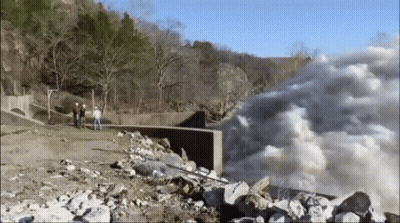 A Group Of People Are Standing On A Rocky Shoreline Looking At A Waterfall . GIF