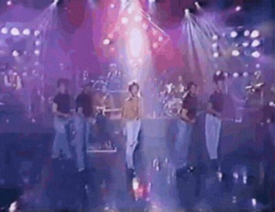 A Group Of People Are Standing On A Stage In Front Of A Stage With Purple Lights . GIF