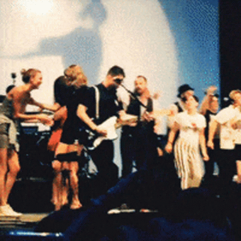 A Group Of People Are Standing On A Stage Playing Guitars GIF