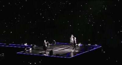 A Group Of People Are Standing On A Stage With A Lot Of Lights On It GIF