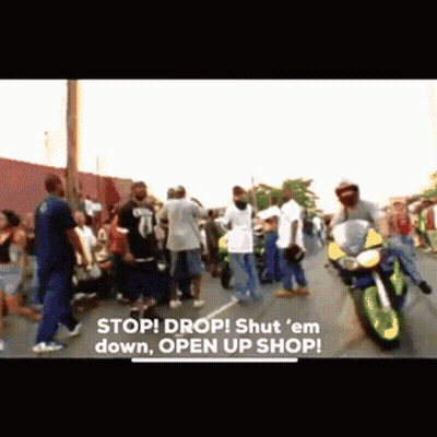 A Group Of People Are Standing On A Street With A Motorcycle In The Foreground And The Words Stop Drop Shut Em Down Open GIF