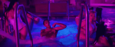A Group Of People Are Swimming In A Swimming Pool At Night . GIF
