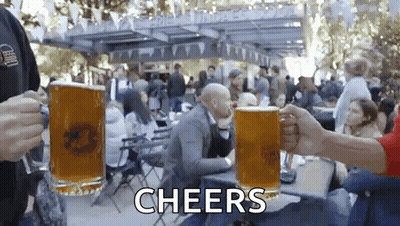 A Group Of People Are Toasting With Beer Mugs And The Words Cheers Are Visible In The Background GIF
