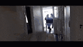 A Group Of People Are Walking Down A Hallway Carrying A Stretcher GIF