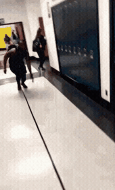 A Group Of People Are Walking Down A Hallway In Front Of A Row Of Lockers . GIF