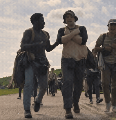 A Group Of People Are Walking Down A Road And One Man Is Holding Another Man 'S Arm GIF
