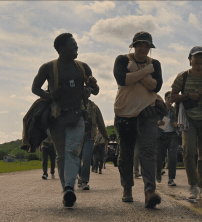 A Group Of People Are Walking Down A Road With One Man Wearing A Shirt That Says ' I 'M A ' GIF