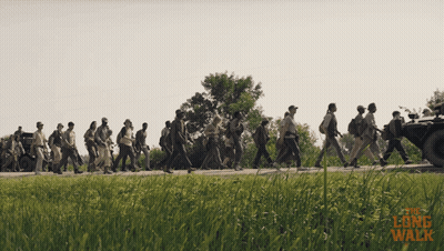 A Group Of People Are Walking Down A Road With The Words " The Long Walk " Written On The Bottom GIF