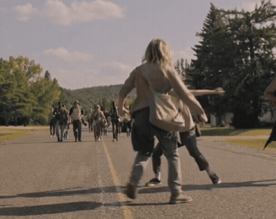 A Group Of People Are Walking Down A Road With Trees In The Background GIF