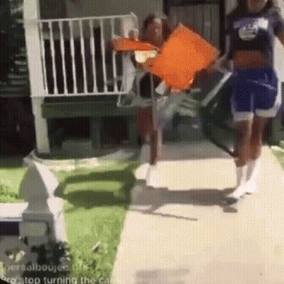 A Group Of People Are Walking Down A Sidewalk And One Of Them Is Holding An Orange Flag . GIF