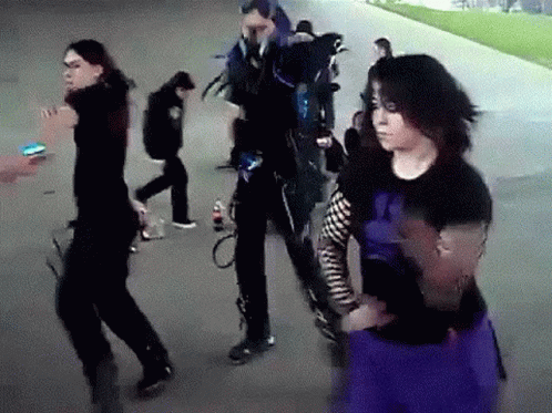 A Group Of People Are Walking Down A Sidewalk And One Of Them Is Wearing A Purple Skirt . GIF