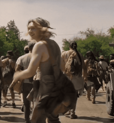 A Group Of People Are Walking Down A Street And A Woman Is Smiling In The Foreground GIF