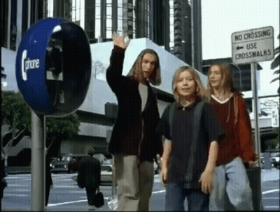 A Group Of People Are Walking Down A Street Next To A Phone Booth And A No Crossing Use Crosswalk Sign . GIF