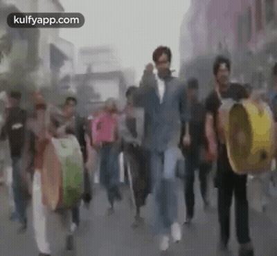 A Group Of People Are Walking Down A Street While Holding Drums . GIF