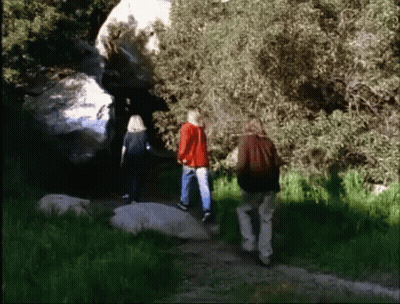 A Group Of People Are Walking In The Woods Near A Rock GIF