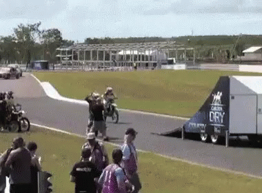 A Group Of People Are Watching A Race On A Track With A Trailer That Says Dry On It . GIF