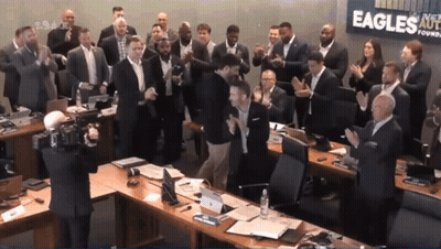 A Group Of People Clapping In Front Of A Sign That Says Eagles On It GIF