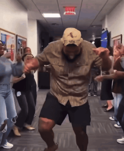 A Group Of People Dancing In A Hallway With A Red Exit Sign Above Them GIF