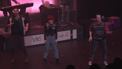 A Group Of People Dancing On A Stage With A Sign That Says Christmas Carols GIF