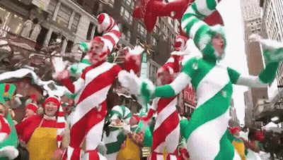 A Group Of People Dressed As Candy Canes Are Dancing In A Parade In A City . GIF