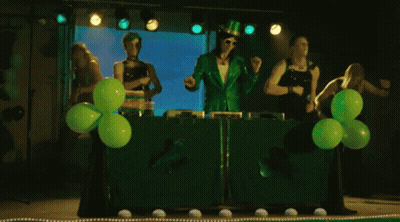 A Group Of People Dressed In Green Are Dancing In Front Of Green Balloons On A Stage GIF