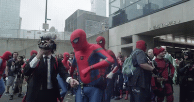 A Group Of People Dressed In Spiderman Costumes Are Walking Down A Street In Front Of A Building That Says Thru Traffic GIF