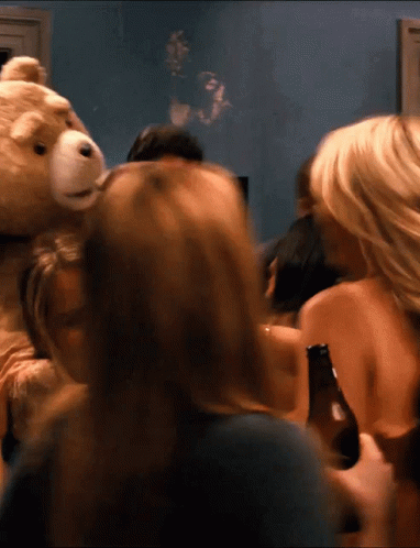 A Group Of People Gathered Around A Teddy Bear Holding A Beer Bottle GIF