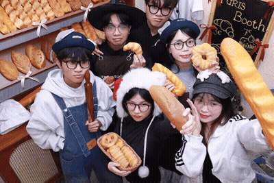 A Group Of People Holding Bread And Donuts In Front Of A Sign That Says ' Turis Booth ' GIF
