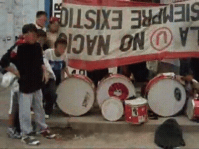 A Group Of People Holding Drums In Front Of A Banner That Says Siempre Existe GIF