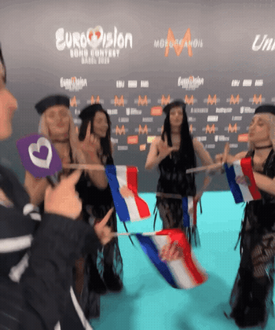 A Group Of People Holding Flags In Front Of A Eurovision Sign GIF