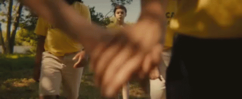 A Group Of People Holding Hands With One Wearing A Yellow Shirt That Says Captain On It GIF