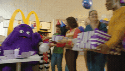A Group Of People Holding Purple Gifts In Front Of A Mcdonald 'S Sign GIF