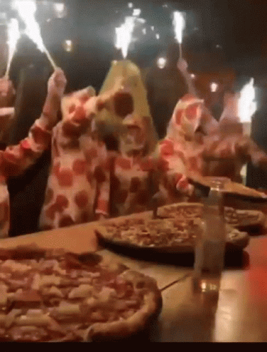 A Group Of People Holding Sparklers In Front Of A Pizza On A Table GIF
