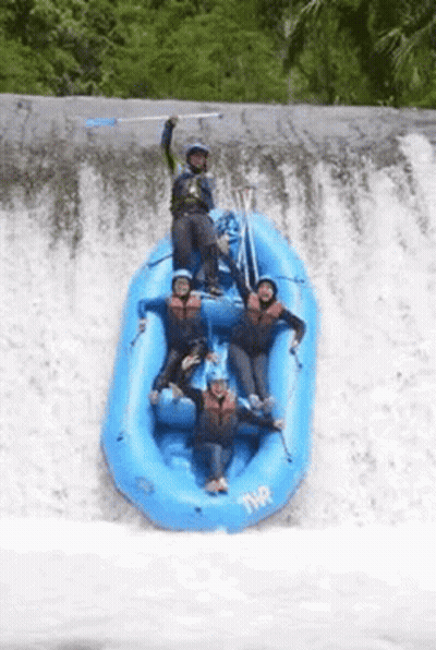 A Group Of People In A Blue Raft Are Standing On Top Of A Waterfall . GIF