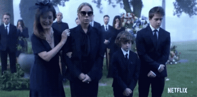 A Group Of People In Black Suits Are Standing In Front Of A Grave . GIF