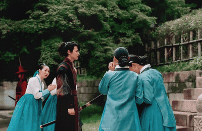 A Group Of People In Blue Dresses Are Standing Around A Man With A Sword GIF