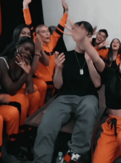 A Group Of People In Orange Jumpsuits Are Sitting Around A Table GIF