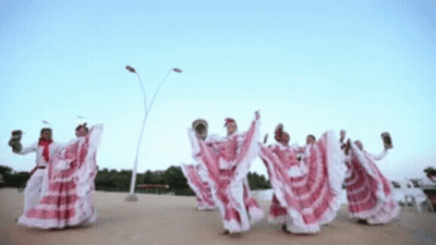 A Group Of People In Red And White Dresses Are Dancing In A Line GIF