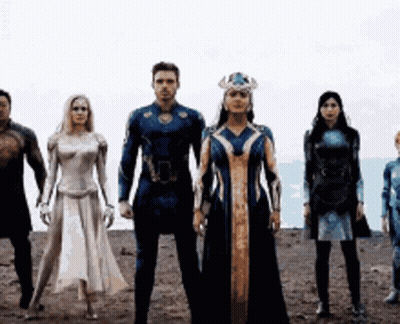 A Group Of People In Superhero Costumes Are Standing Next To Each Other In A Line . GIF