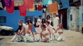 A Group Of People In White Clothes Are Dancing In Front Of A Blue Building GIF