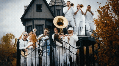A Group Of People In White Playing Instruments In Front Of A House GIF