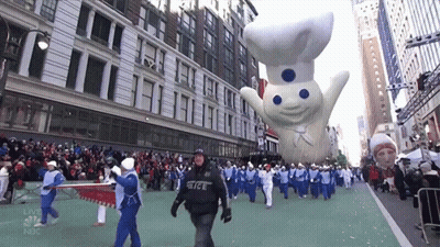 A Group Of People Marching Down A Street With A Nbc Logo In The Background GIF