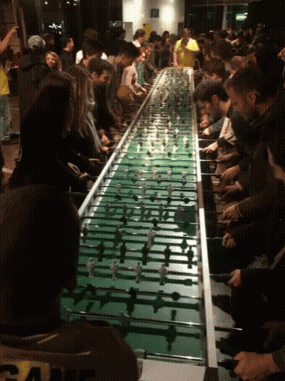 A Group Of People Playing A Game Of Foosball On A Long Table GIF