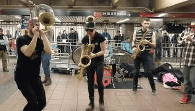 A Group Of People Playing Instruments In Front Of A Sign That Says Exit 34 St & 6Th Avenue GIF